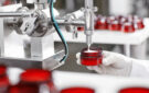 Production and packaging of cosmetics products. Cropped shot of factory worker in gloves and gown holding plastic jar, filling it with white face or body cream. Beauty, skincare and cosmetology